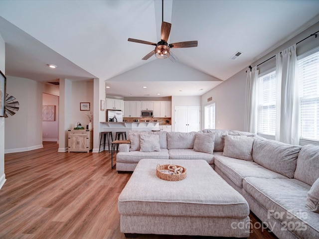 living room featuring ceiling fan, light wood-style flooring, visible vents, baseboards, and vaulted ceiling