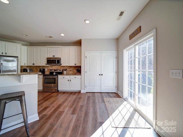 kitchen with stainless steel appliances, wood finished floors, visible vents, white cabinets, and tasteful backsplash