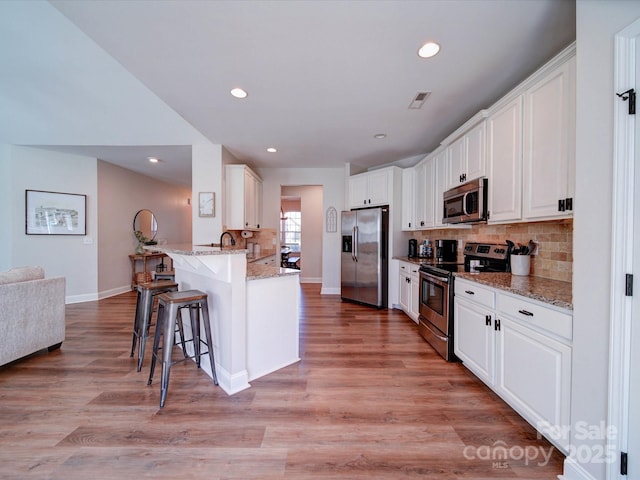 kitchen featuring white cabinets, a peninsula, stainless steel appliances, light wood-type flooring, and a kitchen bar