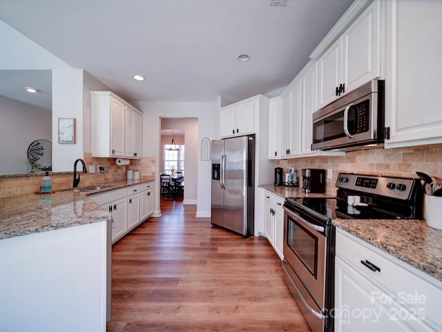 kitchen with appliances with stainless steel finishes, white cabinets, a sink, light stone countertops, and light wood-type flooring