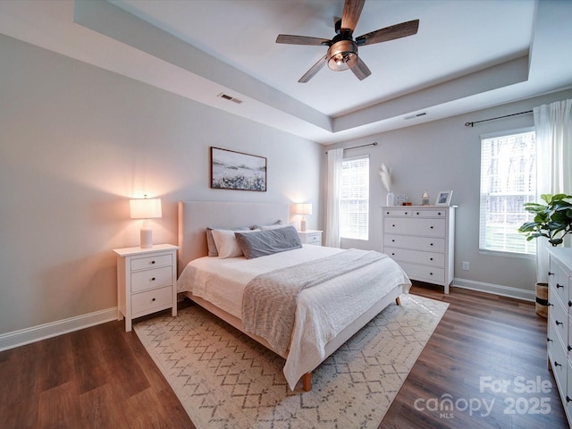 bedroom with a raised ceiling, visible vents, baseboards, and wood finished floors