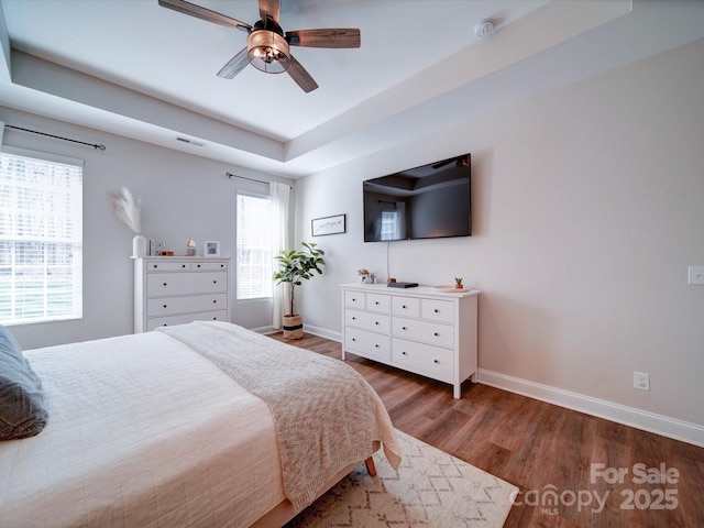 bedroom with baseboards, visible vents, ceiling fan, wood finished floors, and a tray ceiling