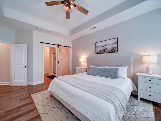 bedroom with a barn door, wood finished floors, visible vents, and baseboards