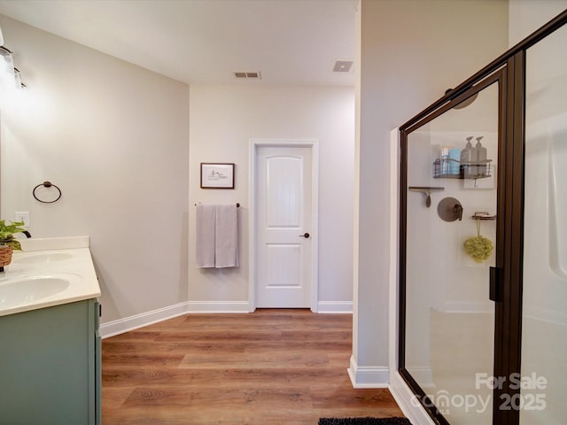 full bath featuring baseboards, visible vents, wood finished floors, a shower stall, and a sink