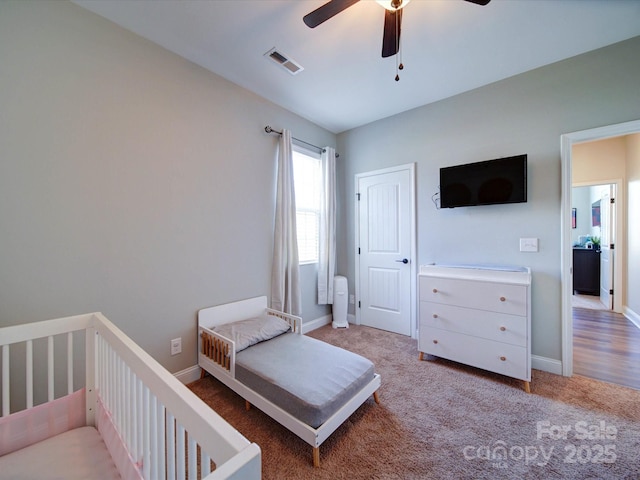 bedroom featuring light colored carpet, a ceiling fan, baseboards, visible vents, and a crib