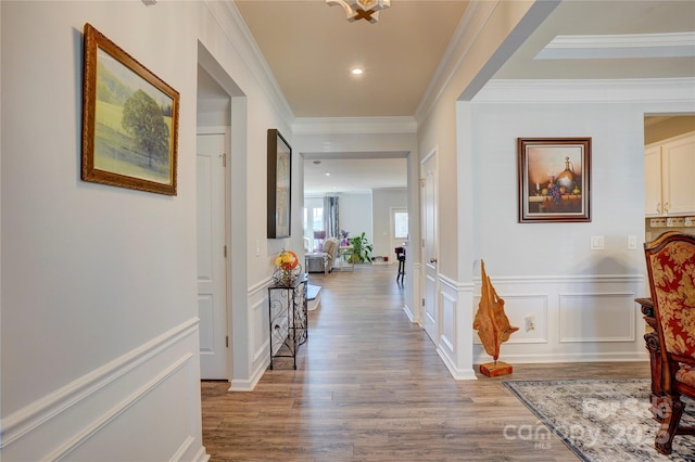 hallway featuring recessed lighting, a decorative wall, wood finished floors, wainscoting, and crown molding