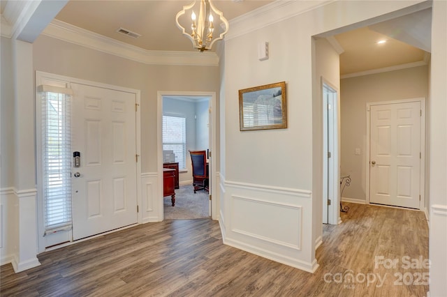 foyer entrance with a wainscoted wall, crown molding, a notable chandelier, visible vents, and wood finished floors