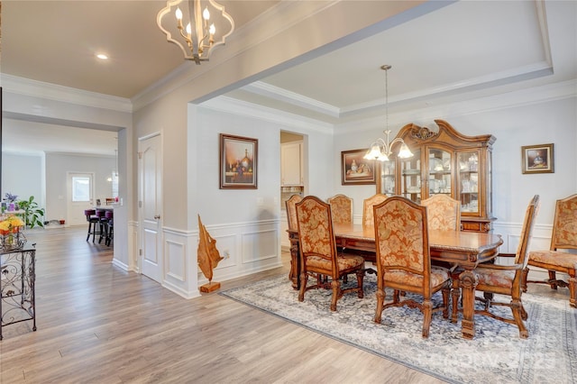 dining space with a tray ceiling, light wood finished floors, and an inviting chandelier