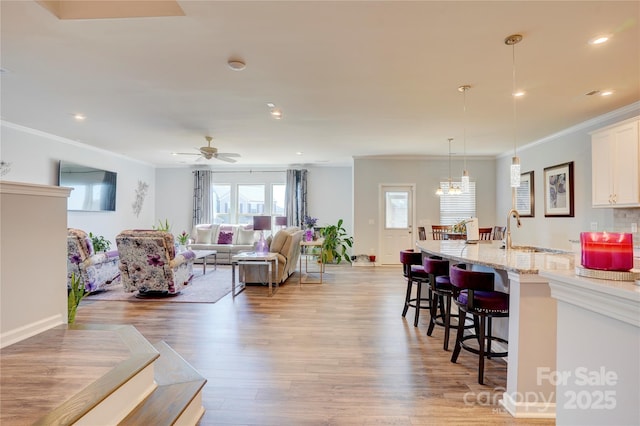 living area featuring light wood-type flooring, ceiling fan, ornamental molding, and recessed lighting