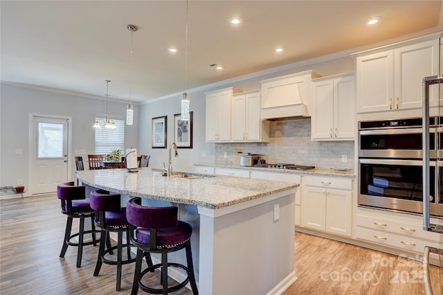 kitchen featuring custom exhaust hood, backsplash, appliances with stainless steel finishes, white cabinetry, and a sink