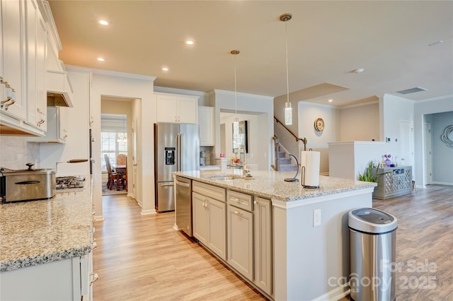 kitchen featuring light wood finished floors, stainless steel appliances, tasteful backsplash, visible vents, and a sink