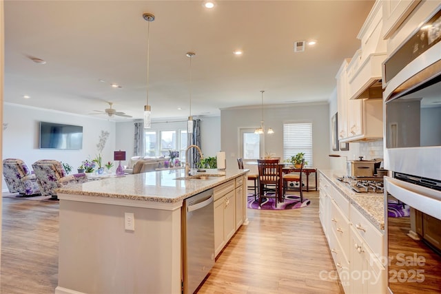 kitchen featuring a center island with sink, stainless steel appliances, light wood-style floors, open floor plan, and a sink