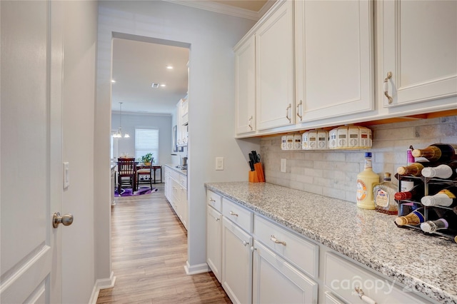 kitchen featuring white cabinetry, light wood-type flooring, backsplash, light stone countertops, and crown molding