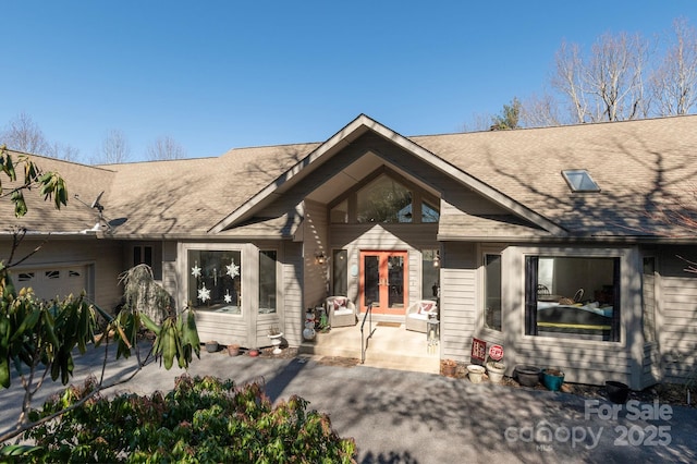 view of front facade featuring a shingled roof, french doors, and an attached garage