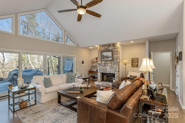 living room featuring a ceiling fan, a stone fireplace, wood finished floors, high vaulted ceiling, and baseboards