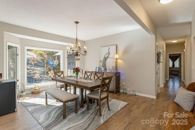 dining area featuring an inviting chandelier, a textured ceiling, baseboards, and wood finished floors