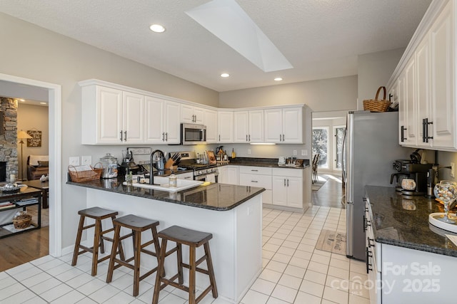 kitchen featuring light tile patterned floors, a peninsula, a skylight, a sink, and appliances with stainless steel finishes