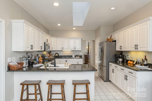 kitchen featuring a peninsula, white cabinetry, appliances with stainless steel finishes, and light tile patterned flooring