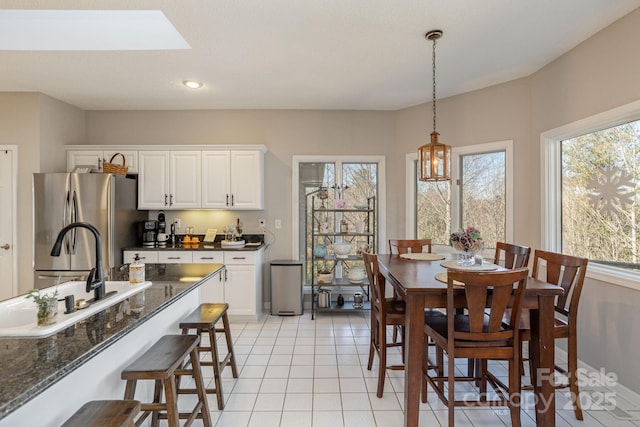 kitchen with a breakfast bar area, hanging light fixtures, freestanding refrigerator, white cabinetry, and light tile patterned flooring