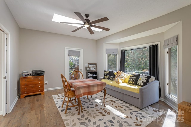 office area with a ceiling fan, light wood-type flooring, baseboards, and a skylight