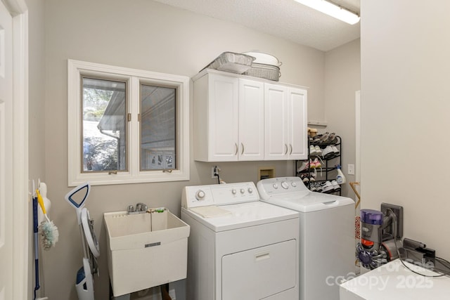 clothes washing area featuring a textured ceiling, washing machine and dryer, a sink, and cabinet space