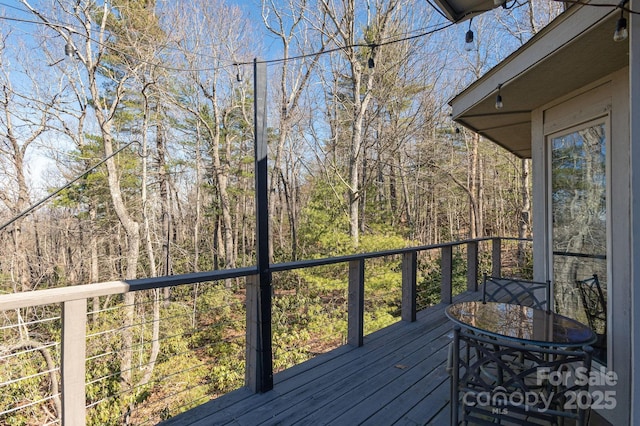 deck with a forest view and outdoor dining area