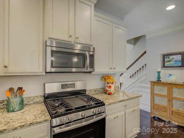 kitchen with appliances with stainless steel finishes, dark wood-type flooring, ornamental molding, and light stone countertops