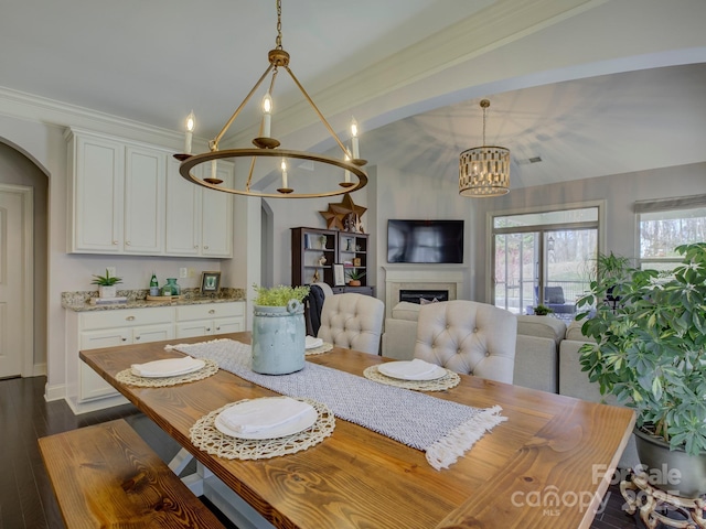 dining area featuring arched walkways, dark wood-type flooring, crown molding, a fireplace, and a notable chandelier