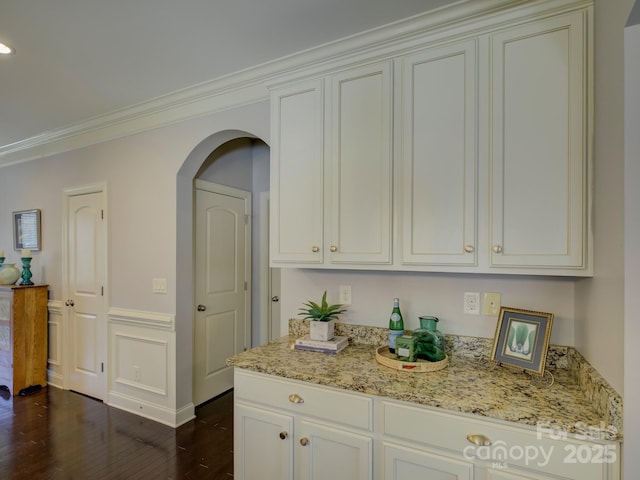 kitchen featuring arched walkways, dark wood-style flooring, crown molding, white cabinetry, and light stone countertops