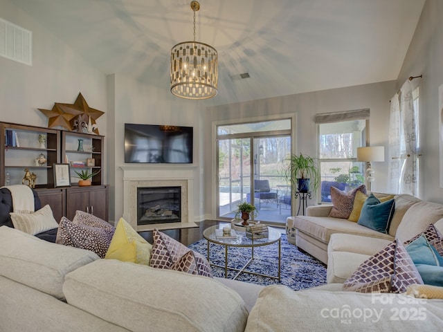 living area with high vaulted ceiling, visible vents, an inviting chandelier, and a glass covered fireplace