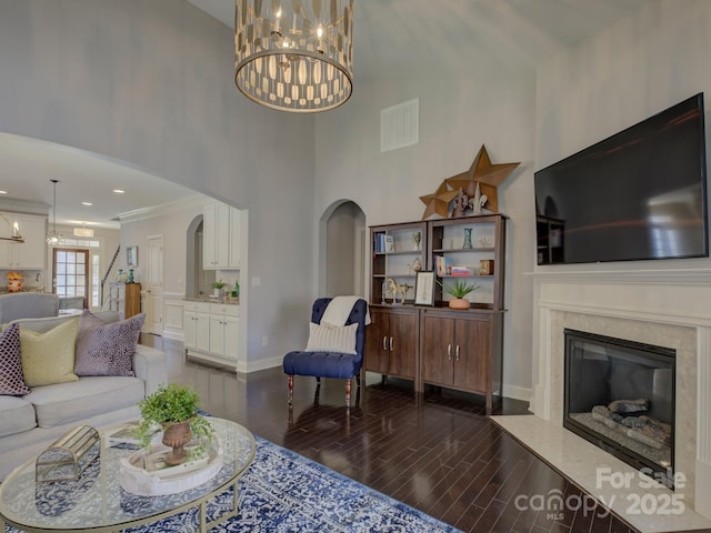 living area featuring visible vents, arched walkways, wood finished floors, an inviting chandelier, and a fireplace