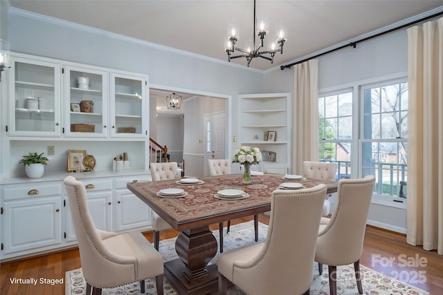 dining space featuring stairway, an inviting chandelier, crown molding, and wood finished floors