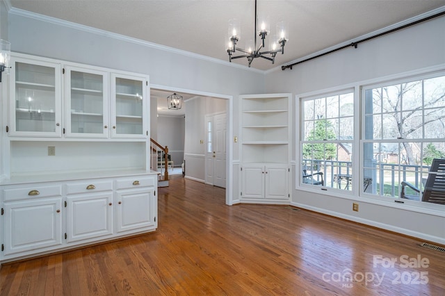 unfurnished dining area featuring ornamental molding, wood finished floors, visible vents, and a chandelier