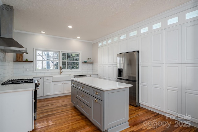 kitchen with gray cabinets, appliances with stainless steel finishes, wall chimney range hood, and open shelves