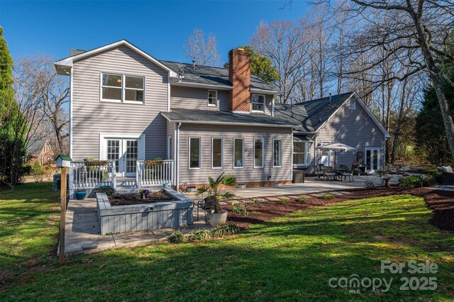 rear view of property featuring french doors, a yard, a wooden deck, a chimney, and a patio area