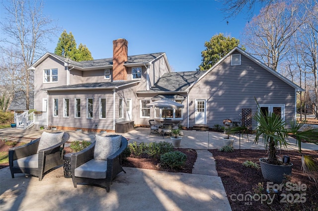 back of house with a chimney, a patio, and roof with shingles