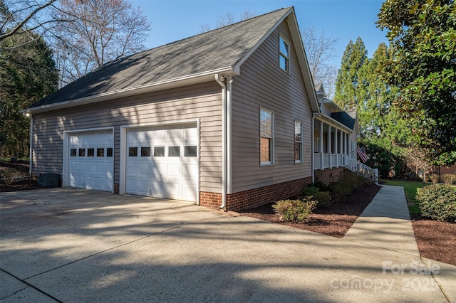 view of side of home featuring concrete driveway, a garage, and roof with shingles