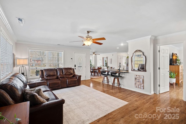 living area with a healthy amount of sunlight, crown molding, baseboards, and wood finished floors