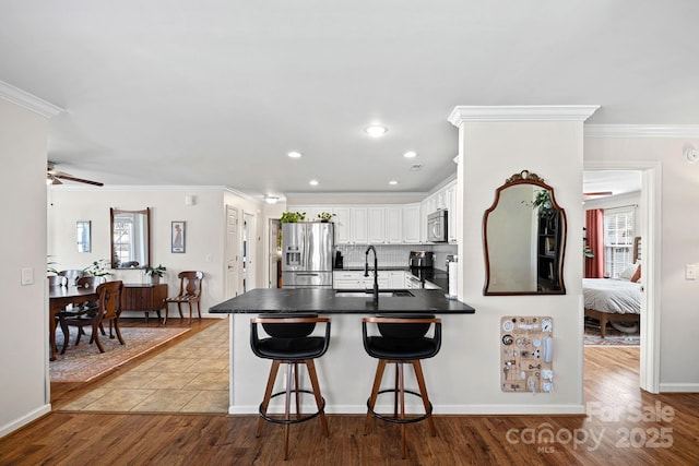 kitchen featuring a peninsula, a sink, appliances with stainless steel finishes, dark countertops, and crown molding