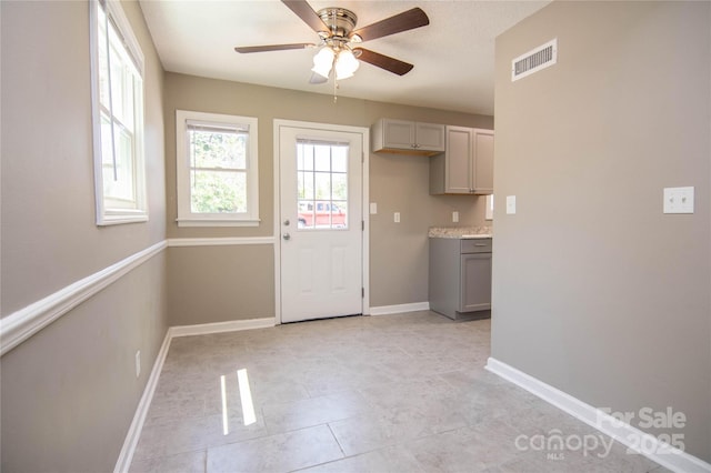 interior space featuring gray cabinetry, a ceiling fan, baseboards, visible vents, and light countertops