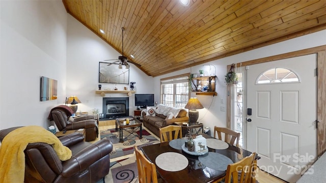 living area featuring a fireplace with raised hearth, high vaulted ceiling, wooden ceiling, and a ceiling fan