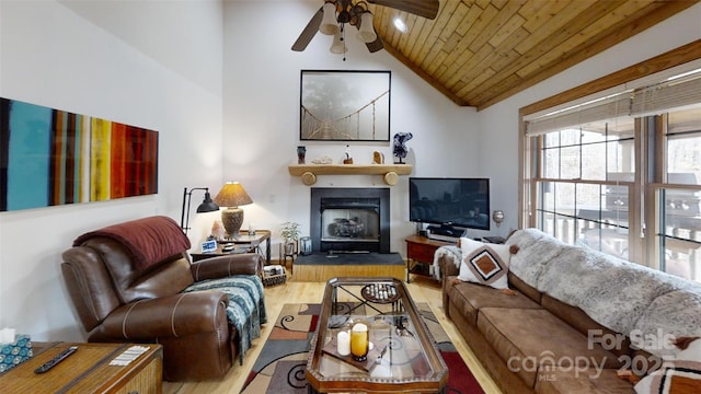 living area featuring a fireplace with raised hearth, wooden ceiling, ceiling fan, wood finished floors, and high vaulted ceiling