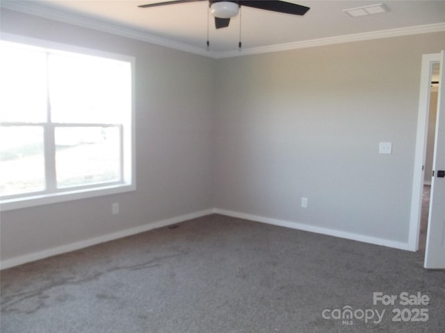 carpeted empty room with a ceiling fan, visible vents, crown molding, and baseboards