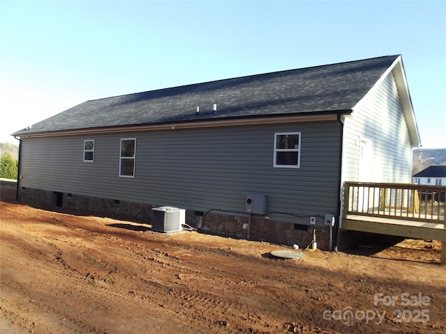 view of side of home with cooling unit, crawl space, roof with shingles, and a deck