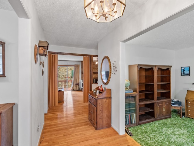 corridor featuring a textured ceiling, light wood-type flooring, and an inviting chandelier