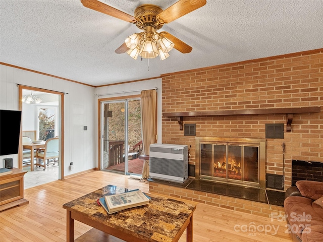 living room with a brick fireplace, crown molding, heating unit, a textured ceiling, and wood-type flooring