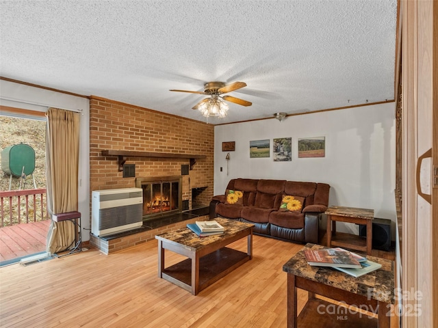 living area featuring heating unit, light wood-style floors, a fireplace, and crown molding