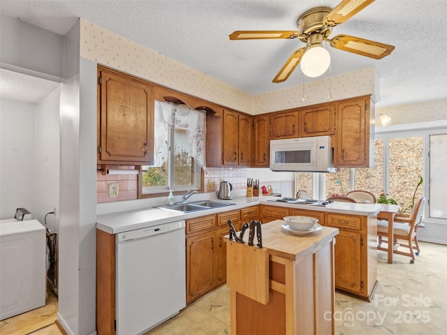 kitchen with white appliances, wallpapered walls, a peninsula, a sink, and a textured ceiling