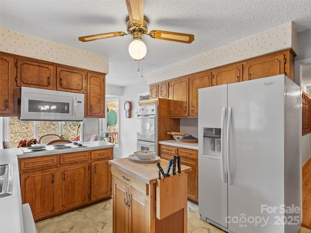 kitchen with white appliances, light floors, wallpapered walls, light countertops, and a textured ceiling