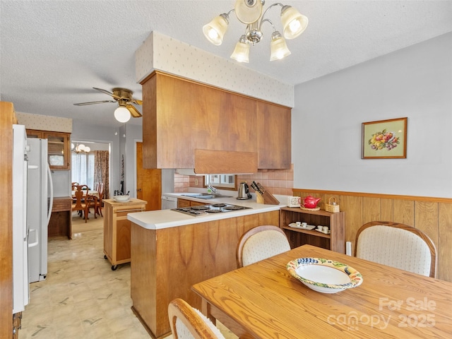 kitchen featuring a peninsula, brown cabinetry, a wainscoted wall, and freestanding refrigerator